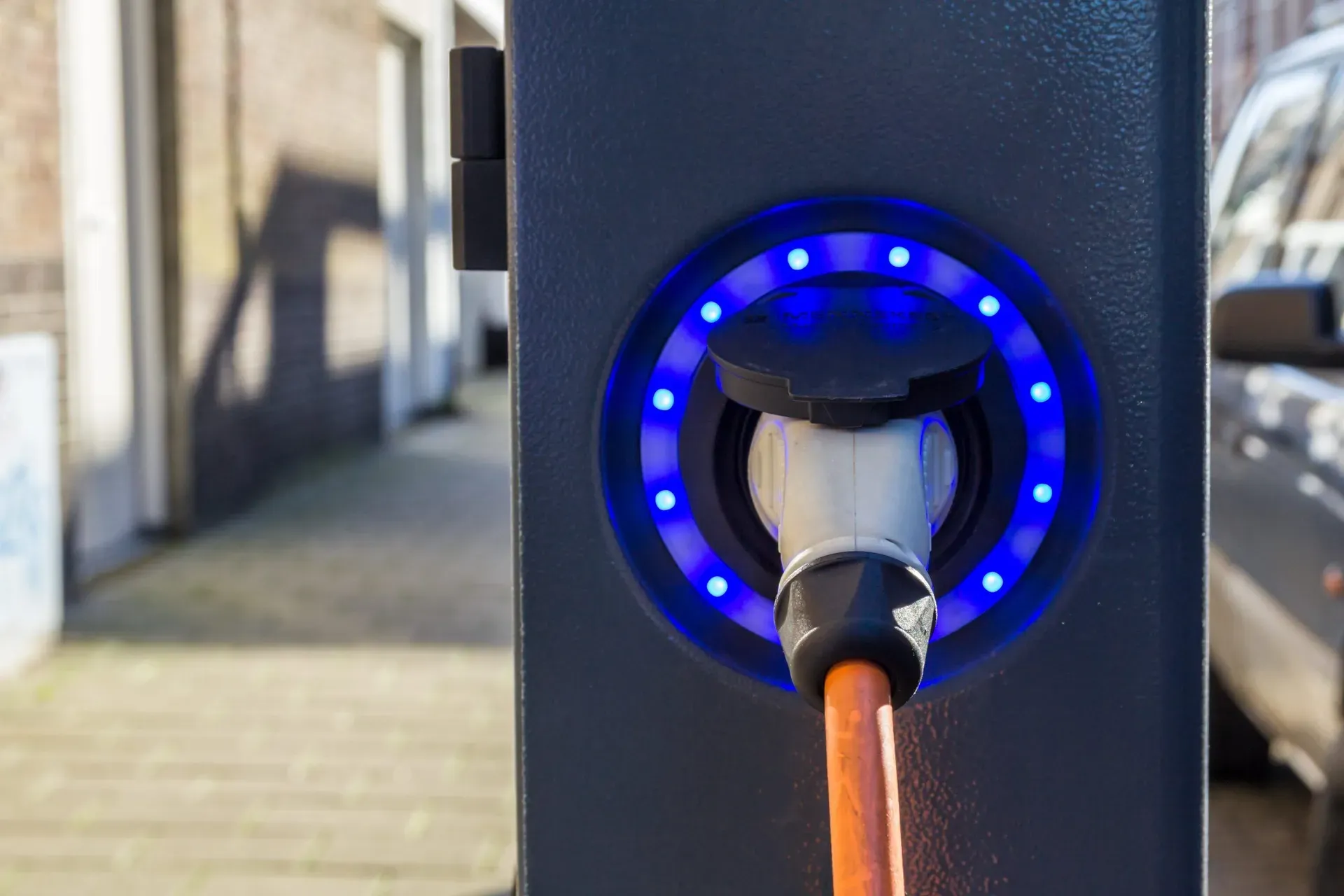 Close-up shot of an electric car charging point with a car in the background.