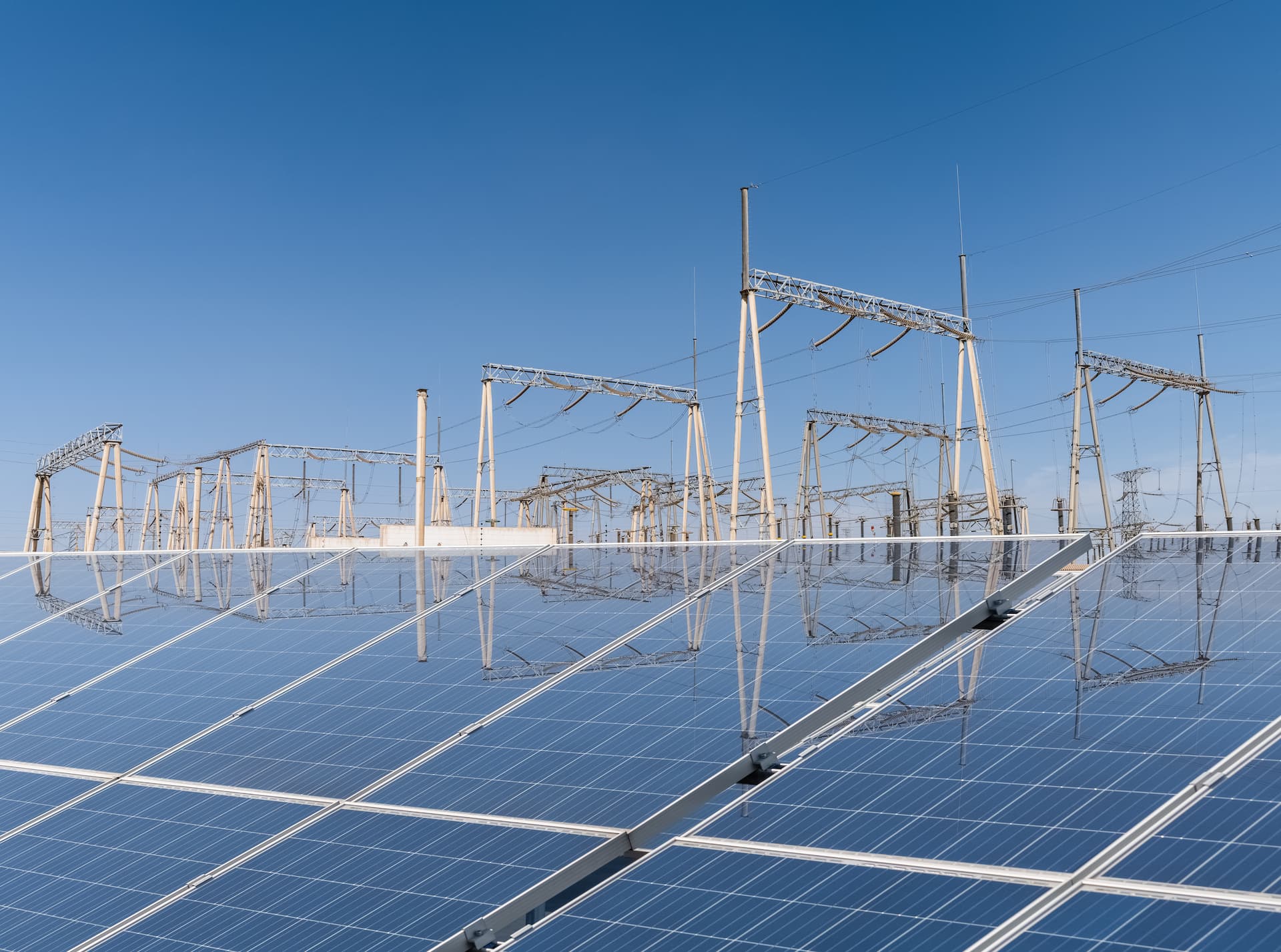 Solar panels in the foreground, with power pylons behind against a blue sky